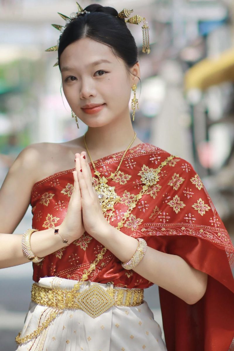 Jeune femme en tenue traditionnelle thaïlandaise saluant d’un wai, dans une rue de Bangkok