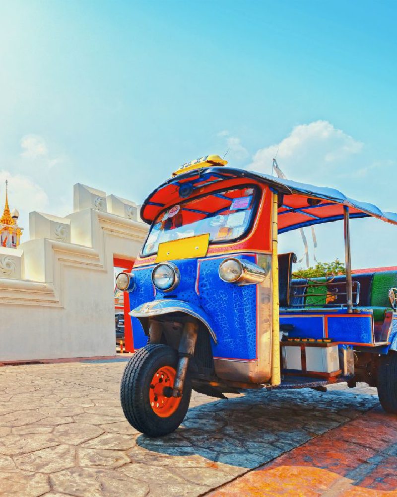 Un tuk-tuk bleu garé devant le mur d’un temple, à Bangkok